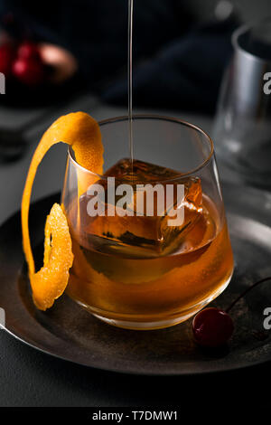 Old fashioned Cocktail in Glas mit großen Ice Cube und orange Swirl garnieren gegossen. Stockfoto