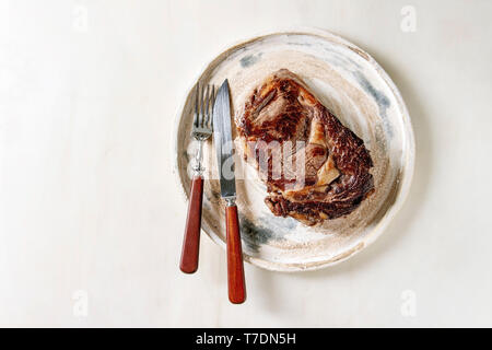 Gegrilltes Rindfleisch Steak gebraten Medium in Keramik Teller mit Besteck mit weißem Marmor Hintergrund serviert. Flach, Raum Stockfoto