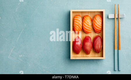 Nigiri Sushi mit Lachs und Thunfisch auf Bambus Platte mit Stäbchen auf blauem Hintergrund serviert. Köstliche traditionelle japanische Küche, Ansicht von oben, flach, Stockfoto