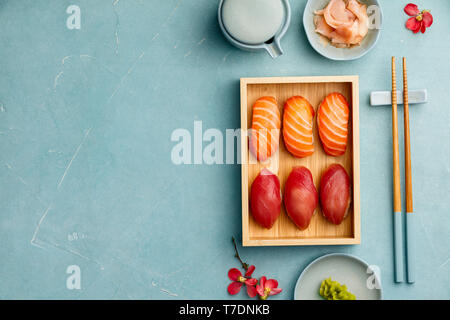 Nigiri Sushi mit Lachs und Thunfisch auf Bambus Platte mit Stäbchen, Soja sause, Wasabi und Ingwer auf blauem Hintergrund serviert. Köstliche traditionelle Japa Stockfoto