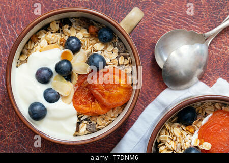 Nahaufnahme der Müsli in eine Schüssel mit getrockneten Aprikosen, Heidelbeeren und Joghurt gekrönt. Stockfoto