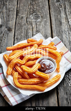 Köstliche Churros mit Schokolade eintauchen auf einem weißen Teller auf einem Holztisch mit Serviette, Traditionelle spanische und mexikanische Street Food, vertikale Ansicht f Stockfoto