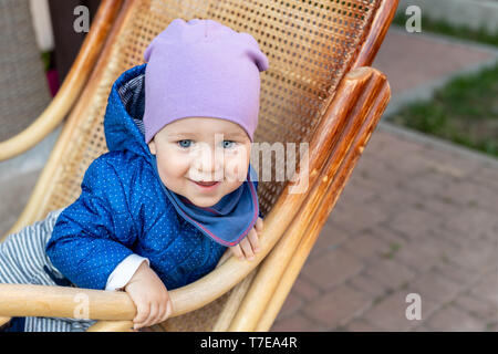 Portrait von cute adorable kaukasische Baby boy Spaß sitzen in Holz rattan Schaukelstuhl auf Haus Terrasse Garten im Freien. Stockfoto