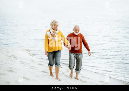 Schönes älteres Ehepaar in bunten Pullover zu Fuß am Sandstrand, genießen freie Zeit im Ruhestand in der Nähe des Meeres gekleidet Stockfoto