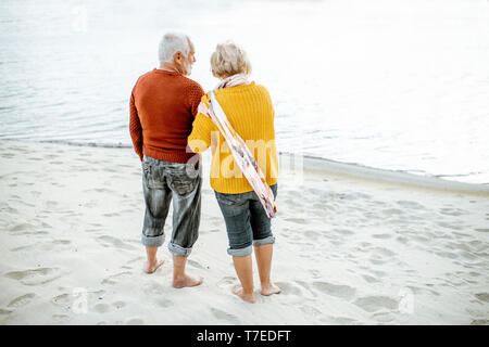 Senior Paar in bunten Pullover Natur geniessen gemeinsam auf dem Sandstrand in der Nähe des Meeres stehen, Rückansicht gekleidet Stockfoto