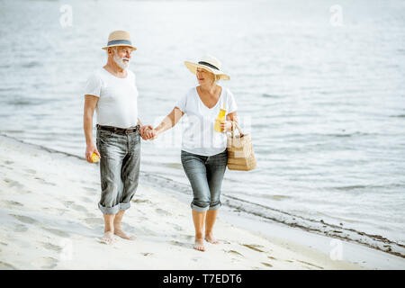 Gerne älteres Paar gekleidet in den weißen T-Shirts und Mützen zusammen zu Fuß am Sandstrand im Ruhestand Stockfoto