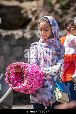 Niasar, Iran, 25. April 2019: Iranische junge Lady mit Blumen, verkaufen Sie an die passbyers stieg während der Erntezeit Stockfoto