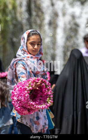 Niasar, Iran, 25. April 2019: Iranische junge Lady mit Blumen, verkaufen Sie an die passbyers stieg während der Erntezeit Stockfoto