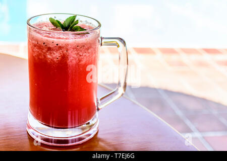 Glas kalte, erfrischende, Rot, Wassermelone Smoothie in Glas mit mint Sprig auf Tisch draußen an einem sonnigen Tag. Stockfoto
