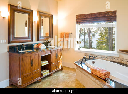 Luxuriöses Badezimmer mit Holz Schränke, Fliesen und Badewanne umgeben, Badewanne und zwei Waschbecken mit hochwertigen Armaturen. Traditionelle Home Interior. Stockfoto