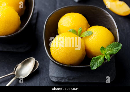 Mango und Pfirsich Eis, Tropical Fruit Sorbet in schwarz Schüssel auf schiefer Hintergrund. Close Up. Stockfoto