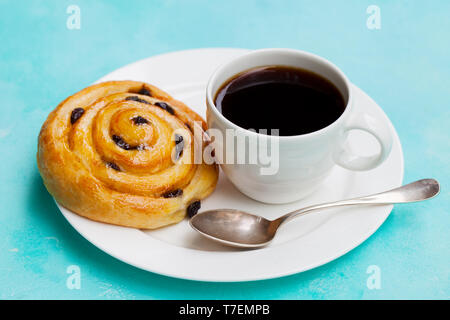 Frischen dänischen Gebäck mit Rosinen und Tasse Kaffee schwarz auf blauem Hintergrund. Close Up. Stockfoto