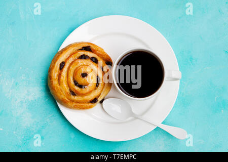 Frischen dänischen Gebäck mit Rosinen und Tasse Kaffee schwarz auf blauem Hintergrund. Ansicht von oben. Kopieren Sie Platz. Stockfoto