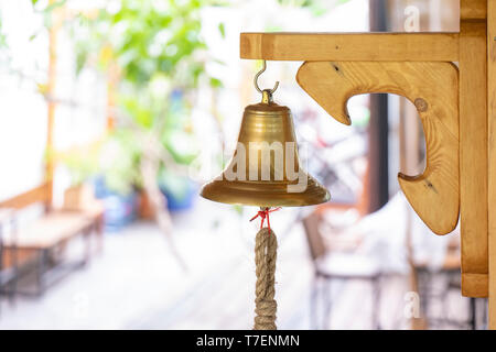 Messing Glocke hand auf zu den hölzernen große Platte Stick auf der Stange an der Wand. Stockfoto