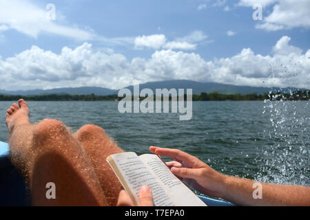 Nahaufnahme DER MANN MIT BUCH UND GENIESSEN SIE DIE SONNE AUF EINER BOOTSFAHRT Stockfoto