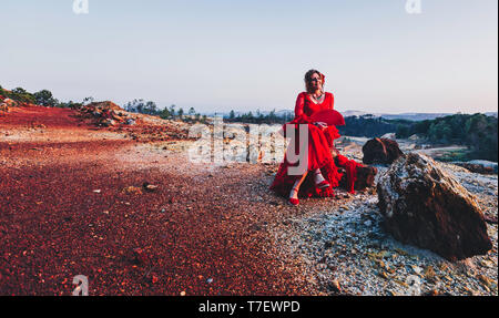 Schöne Frau in Rot flamenco Kleid auf Riotinto Minen sitzt auf einem Stein posing Stockfoto