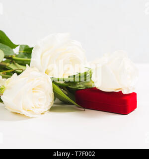 Red Schmuckschatulle mit Blumenstrauß aus den weißen Rosen Valentinstag Konzept mit Gegenwart von Schmuck. Geschenk für die Lieben. Platz schoß Stockfoto