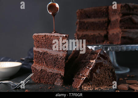 Das Gießen von Schokolade auf Stück leckeren Kuchen auf dem Tisch Stockfoto