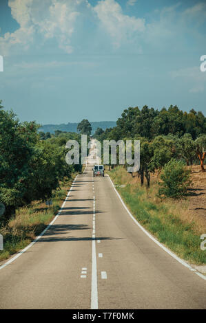 Gerade lange Straße mit einsamen Auto durch Landschaft und belaubten Bäumen, an einem sonnigen Tag in der Nähe von Castelo Branco. Ein ehemaliges Bistum in Zentralportugal. Stockfoto