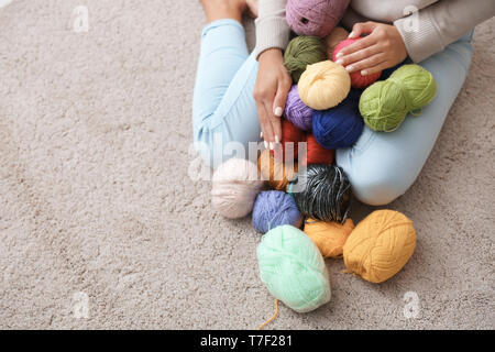 Junge Frau sitzt auf dem Teppich und die Wahl der Farbe des Strickens Gewinde innen Stockfoto