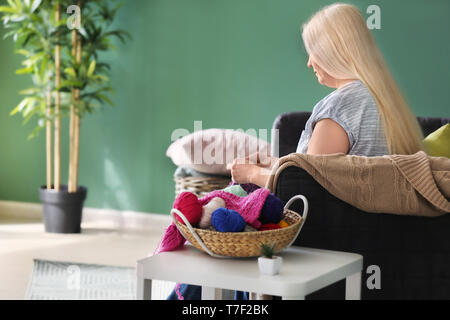 Reife Frau sitzt auf einem Sofa und Stricken warme Pullover im Innenbereich Stockfoto