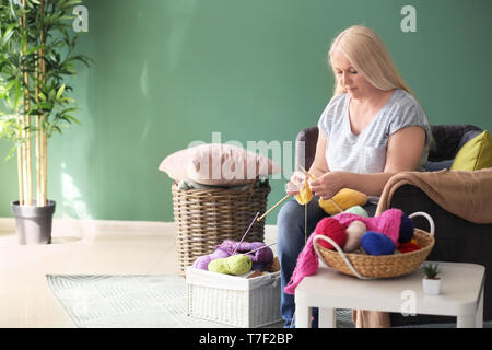 Reife Frau sitzt auf einem Sofa und Stricken warme Pullover im Innenbereich Stockfoto