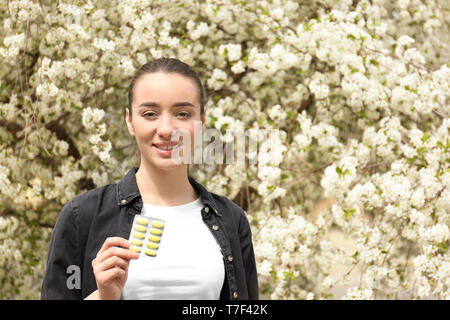 Junge Frau mit Pillen in der Nähe von blühenden Baum. Allergie-Konzept Stockfoto