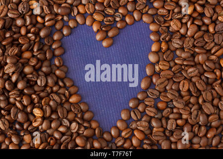 Herz/Rahmen aus Kaffeebohnen auf Violett Textur Hintergrund. Stockfoto