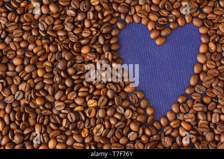 Herz/Rahmen aus Kaffeebohnen auf Violett Textur Hintergrund. Stockfoto