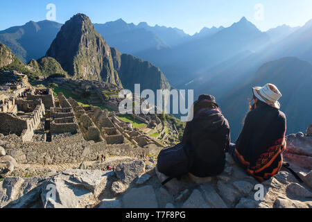Zwei weiße Mädchen sitzen und genießen einen wunderschönen Blick auf die außergewöhnliche archäologische Stätte Machu Picchu, Peru Stockfoto