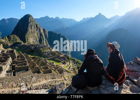 Zwei weiße Mädchen sitzen und genießen einen wunderschönen Blick auf die außergewöhnliche archäologische Stätte Machu Picchu, Peru Stockfoto