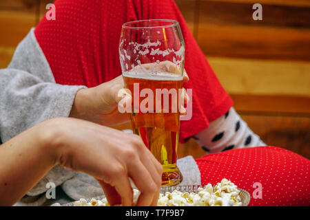 Pint Bier in der Hand mit einer Schüssel Popcorn mit den Schwellen auf Fernsehen zu Hause Stockfoto