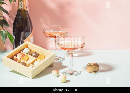 Champagner oder Wein im eleganten Brille, eine Schachtel Pralinen rosa Hintergrund in hellem Licht. Kopieren Sie Platz. Selektive konzentrieren. Stockfoto