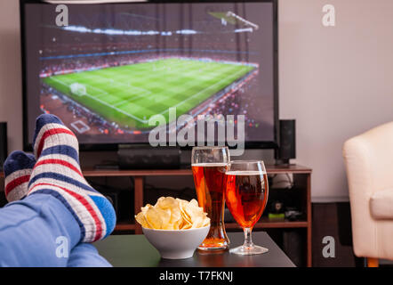 Entspannt Mann lag auf dem Sofa, während Sie Fußballspiel im Fernsehen zu Hause, Bier und Chips auf dem Tisch Stockfoto