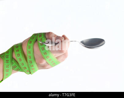 Eine Hand in einem Lineal eingewickelt hält einen Metalllöffel auf einem weißen Hintergrund. Diätetischen Konzept, Gewichtsverlust. Stockfoto