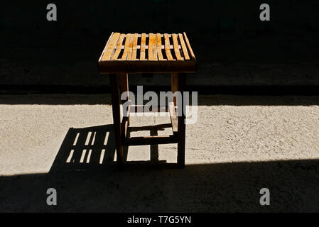 Einen kleinen, einfachen selbstgebauten Tisch aus Holz und Bambus verlassen lange Schatten auf dem sonnenbeschienenen Stock. Die Vorder- und Hintergrund ist schwarz. Stockfoto