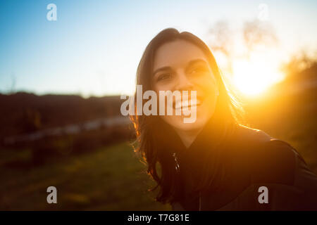 Attraktive junge Frau mit Sonnenuntergang hinter ihr Lachen Stockfoto