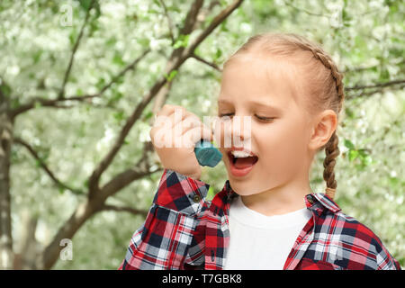 Kleines Mädchen mit Inhalator in der Nähe von blühenden Baum. Allergie-Konzept Stockfoto