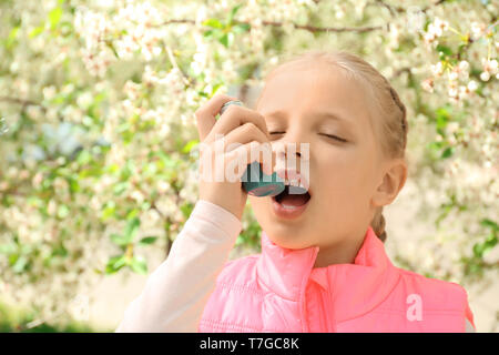 Kleines Mädchen mit Inhalator in der Nähe von blühenden Baum. Allergie-Konzept Stockfoto