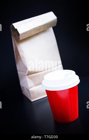 Rote Kaffeetasse und Papiertüte auf schwarzem Hintergrund. Coffee to go Stockfoto