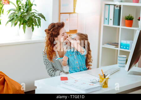 Süße Mädchen berühren Nase von Mutter aus der Ferne zu Hause arbeiten Stockfoto