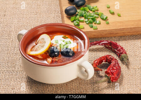 Suppe mit Fleisch saltwort, geräucherte Würstchen, Kartoffeln, Tomaten, Gurken, Zitrone mariniert, schwarzen Oliven und saure Sahne in Keramik Suppenteller, dri Stockfoto