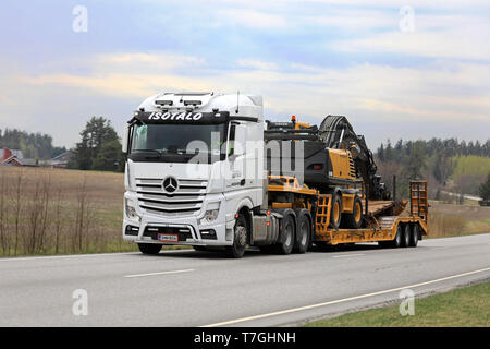 Salo, Finnland - 26 April 2019: Weiße Mercedes-Benz Actros Sattelschlepper von kuljetus Isotalo hols Volvo EW 180 B Mobilbagger mit Rädern auf der Autobahn. Stockfoto