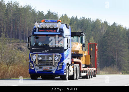 Salo, Finnland - 26 April 2019: Volvo FH 16 750 Auflieger von Lavettikuljetus Ylitalo & Vahtera Oy hols Cat CW 34 Gummiradwalze entlang der Autobahn. Stockfoto