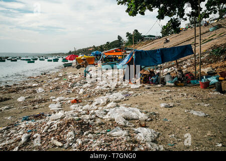 Vietnamesische Frau wirft Müll auf der Strand am Meer. Durch das Meer Dump. Schlechte Ökologie in Südostasien. Fischer Dorf in Mui Ne, Vietnam Stockfoto