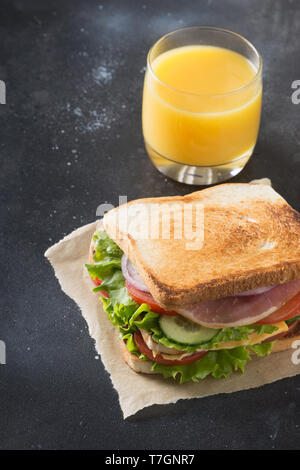 Orangensaft und Sandwich und mit Speck, Tomaten, Zwiebeln, Salat auf schwarzen Hintergrund. Close Up. Fast food. Stockfoto