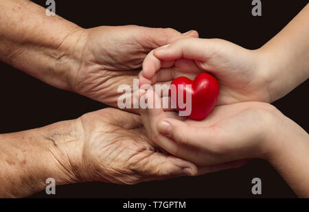 kleine Mädchen und ältere Frau rotes Herz in ihre Handflächen zusammen, Symbol der Liebe und Sorgfalt zu halten Stockfoto