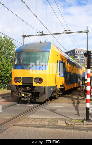 Niederländische Bahn Multiple Unit Train in NS-blaue und gelbe Lackierung auf einem Bahnübergang in Leiden auf Donnerstag, den 25. April 2019. Stockfoto