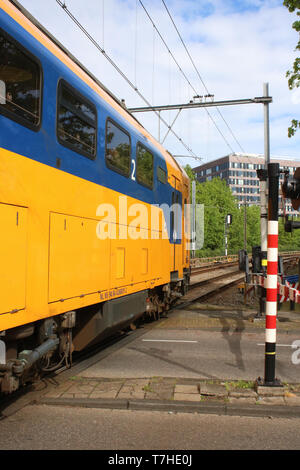 Niederländische Bahn Multiple Unit Train in NS-blaue und gelbe Lackierung auf einem Bahnübergang in Leiden auf Donnerstag, den 25. April 2019. Stockfoto