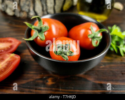 Tomaten in einem schwarzen Schale, Olivenöl und Petersilie auf dunklem Holz Tisch Stockfoto